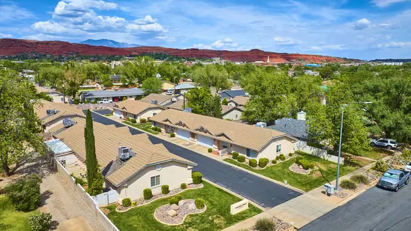 St. George Utah 'ta sakin bir banliyö mahallesinin havadan görünüşü. Düzenli sıva evler, manikürlü çimenler ve parlak parçalı bulutlu gökyüzünün altında muhteşem kızıl kaya birikimleri.
