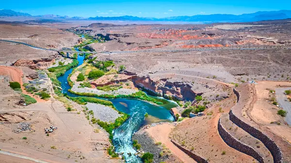 Las Vegas Gölü yakınlarındaki çölden akan turkuaz bir nehrin hava manzarası. Kayalık kanyonlar boyunca uzanan bir köprü ve sular boyunca canlı yeşil bir bitki örtüsü.
