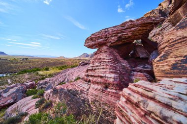 Las Vegas Nevada yakınlarındaki Red Rock Kanyonu 'nun üzerinde Calico Tepeleri ve açık mavi gökyüzünün altındaki uzak dağlarla dramatik katmanlı kumtaşı kayaları dengede duruyor.
