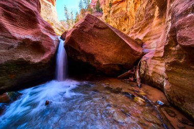 Huzurlu bir şelale Kanarra kanyonundaki kırmızı kayaların arasından akar. Utah kanyonu kumtaşı uçurumlarını aydınlatır. Amerika 'nın güneybatısında sakin bir doğa macerası sahnesi için.
