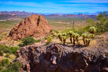 Phoenix Arizona yakınlarındaki Kayıp Hollandalı Eyalet Parkı 'nın canlı manzarası. Güneşli ön planda yüksek kızıl kaya oluşumları ve berrak mavi gökyüzünün altında görkemli çöl dağları.