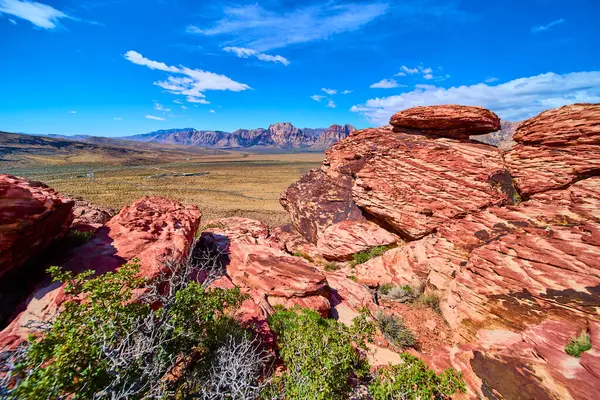 Kızıl Kaya Kanyonu 'nun canlı kırmızı kumtaşı oluşumları geniş Nevada çölüne karşı Calico Hills ve engebeli dağların altında macera ve seyahat temaları için mükemmel mavi gökyüzü altında duruyor.