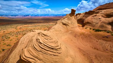 Arizona Sayfası yakınlarındaki dramatik kumtaşı oluşumlarının hava görüntüsü. Gün ortası güneşinde parlayan katmanlı amfi tiyatro şekilleri, canlı mavi gökyüzü ve Amerika 'nın güneybatısında geniş bir çöl manzarası.