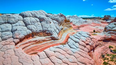 Arizona Vermilion Cliffs Ulusal Anıtı 'ndaki Beyaz Cep' in havadan görünüşü çarpıcı bir çöl manzarasında berrak mavi gökyüzü altında parlak katmanlı kumtaşı oluşumlarını sergiliyor.