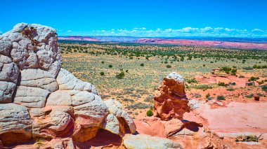 Arizona 'daki Vermilion Cliffs Ulusal Anıtı' ndaki White Pocket 'daki engebeli kaya oluşumlarının hava görüntüsü. Açık mavi gökyüzünün altında canlı kumtaşı dokularıyla dramatik çöl manzarası..