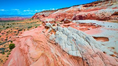 Vermilion Cliffs Ulusal Anıtı Arizona 'daki White Pocket' daki canlı kırmızı ve beyaz kaya oluşumlarının havadan görüntüsü. Açık mavi gökyüzü altında geniş çöl manzaraları ve uzak mesafelere sahip.