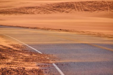 Sand Hollow Eyalet Parkı 'ndaki altın kum tepeleri boyunca kıvrılan dolambaçlı bir yol, Birleşik Devletler yakınlarındaki engin çöl manzarası boyunca seyahat etmenin yalnızlığını ve macerasını yakalıyor.