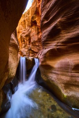 İpeksi şelale Kanarra kanyonu Utah 'ın düz kumtaşı duvarlarından akar. Dramatik ışık ve sakin su, güneybatı macerası ve doğa harikası için çarpıcı bir manzara yaratır..