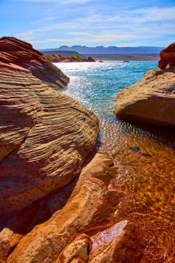 Güneşli kumtaşı oluşumları Utah 'taki Sand Hollow State Park Gölü' nün berrak mavi sularıyla buluşuyor. Parlak gökyüzü altında uzak mesafelere sahip dağlar, Amerika 'da macera ve sükuneti çağrıştırıyor.
