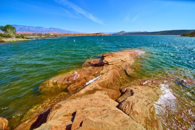 Turkuaz sular Utah Kasırgası 'ndaki Sand Hollow Eyalet Parkı' nda dramatik kırmızı kayalarla buluşur. Güneşli gökyüzünün altında uzak dağlar açık hava macerası ve yaz rahatlaması için mükemmel bir manzara yaratır.