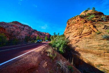 Dolambaçlı bir yol Zion Ulusal Parkı Utah 'ta açık mavi bir gökyüzünün altındaki parlak kırmızı kumtaşı uçurumlarına çıkar. Bu klasik Amerikan Güneybatısındaki birçok havuz patikasında iki araba seyahat eder.
