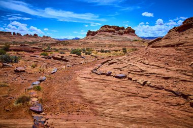 Çizgili kırmızı kumtaşı oluşumları engebeli çöl arazisinin üzerinde yükseliyor ve canlı mavi bir gökyüzü altında Arı Kovanı Patikası boyunca Arizona yakınlarında Amerikan Güneybatısının güzelliğini yakalıyor.