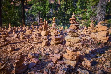 Rock stacks called cairns line a sunlit path in Bryce Canyon National Park Utah with pine trees in the background along the Queens Garden and Navajo Loop trails creating a sense of balance and outdoor