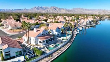 Havadan Uçarak İlerlemek: Terracotta-çatı evleri, bereketli palmiye ağaçları ve görkemli bir gökyüzü altında uzanan görkemli dağlara karşı kurulu sakin göl manzaralı lüks Las Vegas yerleşim yerlerini keşfetmek