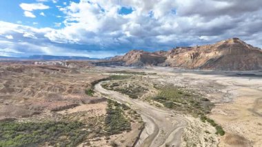 Rüzgarlı bir nehir yatağının üzerinde uçan ve Arizona Sayfası yakınlarındaki dramatik çöl dağlarının üzerinde dinamik bir gökyüzü altında yemyeşil alanlar nefes kesici bir çekim yaratıyor..