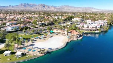 Aerial Fly through Forward: kırmızı kiremitli evler, yemyeşil verimli bir göl ile huzurlu bir Las Vegas banliyösü keşfetmek, hepsi açık mavi gökyüzü altında görkemli dağların zemin karşı kurulmuş.