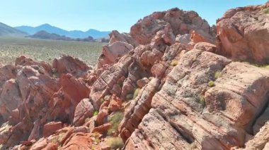 Whitney Pocket yakınlarındaki Nevadas Gold Butte Ulusal Anıtı 'ndaki çarpıcı kırmızı kumtaşı oluşumlarının üzerinden uçarak geçerler engebeli kayalar çöl bitkileri ve açık mavi gökyüzü altındaki uzak dağlar..