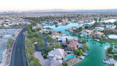Havadan İzleme Çekimi: Las Vegas 'ta lüks, lüks evler, yemyeşil alanlar ve altın saat boyunca sakin bir göl keşfedin..