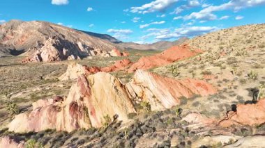 Havadan çekilen görüntüler, dağınık Joshua ağaçları ve Nevadas Gold Butte Ulusal Anıtı 'ndaki uzak dağlarla canlı kırmızı ve bronz kaya oluşumlarının üzerinde süzülerek Whitney' in engebeli güzelliğini yakalıyor.