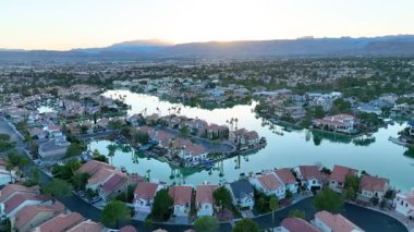 Aerial Fly Over: Gün doğumunda sakin bir Las Vegas göl kenti topluluğu keşfedin. Zarif evlere, sakin sulara ve görkemli dağların zeminine kurulmuş palmiye kaplı sokaklara hayret..