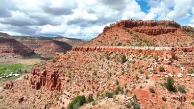Kanab Utah 'taki dramatik kırmızı kaya tepecikleri ve kanyon arazisinde, dinamik bulutlar ve canlı çöl renkleriyle uçarak aşağıdaki geniş araziyi ve şehri bir ileri çekim ile yakalıyor..