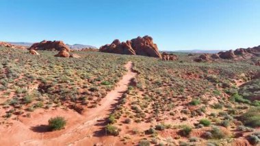 St. George yakınlarındaki Utah 'taki kızıl uçurumlar ve dolambaçlı çöl patikalarında uçan hava, açık bir gökyüzü altında canlı kayalar ve seyrek bitki örtüsüyle Kızıl Kayalıklar' ın engebeli güzelliğini yakalar..