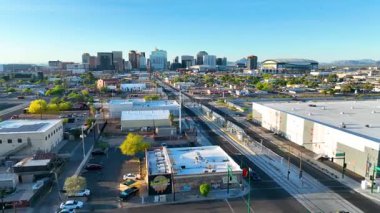 Phoenix Arizona şehir merkezindeki havadan uçuşta şehrin ufuk çizgisi gün ışığında hafif tren rayları ve stadyumu ileri hareket perspektifli enerjik bir kentsel çekim yaratıyor..