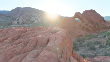 Bunkerville Nevada yakınlarındaki Gold Butte Ulusal Anıtı 'nda kumtaşı ve engebeli araziyi aydınlatan altın gündoğumu ışıklarıyla dramatik kırmızı kaya kemeri ve çöl manzarasının içinden uçarak geçerler..