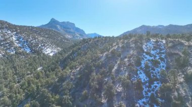 Havadan Uç İleriye: Las Vegas yakınlarındaki Charleston Dağı 'nın görkemli güzelliğini tecrübe edin. Berrak mavi gökyüzünün altında karla kaplı tepeler ve yemyeşil ormanlar sakin ve geniş bir doğal manzara yaratır..