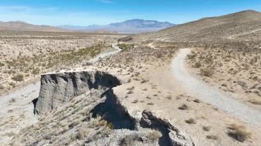 İleri Uçan Havadan Uçan Dağ 'ın engebeli güzelliğine hayran olun. Charleston, Nevada, kamera kayalık çıkıntılar üzerinde süzülürken ve engin mavi gökyüzünün altında dolambaçlı yollar, sakin bir çöl manzarasını ortaya çıkarıyor..