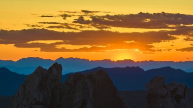 Engebeli kaya oluşumları ve uzak sıradağlar, altın saat boyunca Nevada 'da, Gold Butte Ulusal Anıtı' nda gün batımında canlı bir gökyüzünün altında parlıyor.