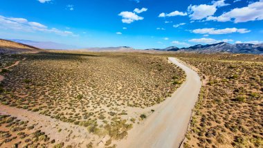 Nevadas 'ın engebeli arazisine uzanan dolambaçlı bir çöl yolunun havadan görünüşü. Arka planda Charleston dağı ve yukarıda parlak mavi gökyüzü var..