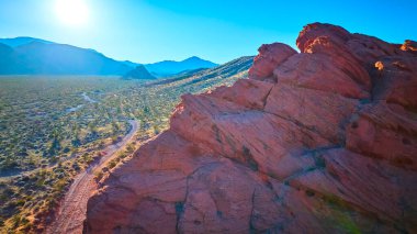 Altın Kasap Ulusal Anıtı Nevada 'daki dolambaçlı bir çöl yolunun üzerinde kızıl kumtaşı uçurumları yükseliyor. Güneş ışığı, geniş araziyi ve uzak sıradağları aydınlatıyor.
