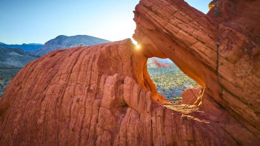 Altın saat ışığı Nevadas Altın Kalça Ulusal Anıtı 'nda çarpıcı bir kemer oluşumundan akıyor. Engebeli kırmızı kayalar ve engin bir çöl dramatik bir hava manzarası yaratıyor.