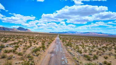 Uçsuz bucaksız çöl yolu manzarası mavi gökyüzü ve dağınık bulutlar ile uzak dağlara doğru gidiyor. Macera dolu yalnızlık ve açık alan.