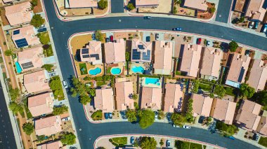 Arka bahçeli havuzlu evler ve güneş panelleri parlak çöl ışığı altında kıvrımlı sokaklar.