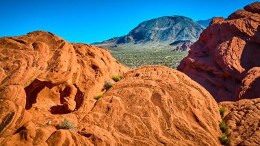 Doğal kemerli parlak kırmızı kumtaşı kayaları ve seyrek bitki örtüsü engebeli bir dağ ve geniş bir çöl. Altın Göt Ulusal Anıtı Nevada 'da, açık mavi gökyüzünün altında.