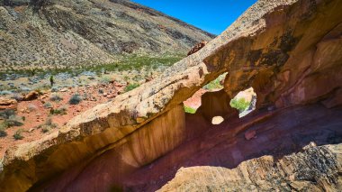 Whitney Pocket 'da kırmızı kaya oluşumu belirgin bir şekilde duruyor. Etrafı Nevada' nın engebeli çöl arazisi ve açık mavi gökyüzünün altında bulunan nadide bitki örtüsüyle çevrili.