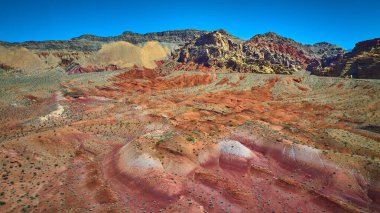 Altın Butte Ulusal Anıtı 'nın havadan görünüşü katmanlı kırmızı kumtaşı tepeleri engebeli dağlar ve açık mavi gökyüzünün altında seyrek çöl bitkileri gösteriyor.