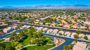 Açık gökyüzünün altında yeşil bir parkı çevreleyen evler ve uzak dağlar manzaralı bir zemin oluşturuyor.