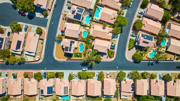 Las Vegas 'ın güneşli bir mahallesinde havuz, güneş panelleri ve ağaç gölgeli caddelerle dolu banliyö evlerinin tepeden aşağı manzarası.