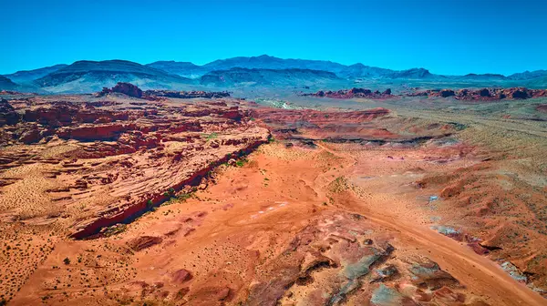 Uçsuz bucaksız kızıl kaya oluşumları çöl düzlükleri ve açık mavi gökyüzünün altındaki uzak dağlar Altın Göt Ulusal Anıtı 'nın engebeli güzelliğini yakalıyor.