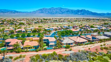 Zengin peyzaj ve havuzlu varoş evlerinin geniş manzarası çarpıcı bir çöl arkaplanına kurulmuş.