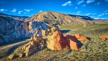 Renkli Whitney Pocket kaya oluşumlarıyla Nevada 'daki Gold Butte Ulusal Anıtı' nın çarpıcı hava manzarası açık mavi gökyüzünün altında çöl bitki örtüsü ve dağ arkaplanı