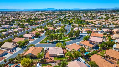 Barışçıl evlerin, yeşil parkın ve açık mavi gökyüzünün altındaki uzak şehrin geniş bir hava manzarası.