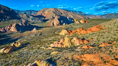 Whitney Pocket 'in eşsiz kırmızı ve sarı kaya oluşumları ve canlı mavi gökyüzü altında engebeli Nevada çöl dağlarının yer aldığı Altın Kalça Ulusal Anıtı' nın geniş hava manzarası.