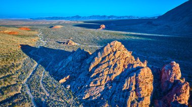 Güneşli kaya oluşumları Nevada 'daki uçsuz bucaksız Gold Butte Ulusal Anıt Çölü' nün üzerinde Whitney Pocket ve altın saat boyunca aydınlatılmış uzak dağlarla durmaktadır.