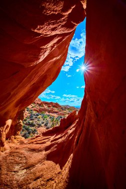 Güneş ışığı, Whitney Pocket 'deki kırmızı bir kaya kemeri oluşumundan akar. Nevada' daki Gold Butte Ulusal Anıtı 'nda engebeli çöl manzarası ve arka planda mavi gökyüzü vardır.