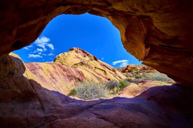 Canlı Napolitan kemer oluşumu Whitney Pocket Nevada yakınlarındaki Gold Butte Ulusal Anıtı 'nda açık mavi gökyüzünün altında renkli kumtaşı tepeleri ve çöl bitkilerini çerçeveler.