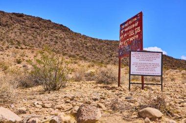 Yıpranmış tabela ve engebeli kayalar Amerika Birleşik Devletleri 'nde açık mavi gökyüzü altında seyrek Nevada bitki örtüsü bulunan Altın Butte Ulusal Anıtı çölünün ortasında göze çarpıyor.